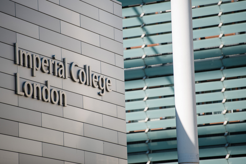 A close up of the Imperial College London name on the side of a modern building, with a modern glass building behind it.